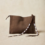 Small sand brown suede leather pouch bag with white, black, and red beaded zipper pull ties on a sand background