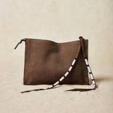 Small sand brown suede leather pouch bag with white, black, and red beaded zipper pull ties on a sand background