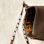 Detailed view of the colorful kanga fabric lining of the small sand brown suede leather pouch bag with white, black, and red beaded zipper pull ties on a sand background