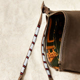 Detailed view of the colorful kanga fabric lining of the small sand brown suede leather pouch bag with white, black, and red beaded zipper pull ties on a sand background