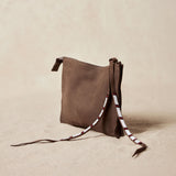 Alternative diagonal view of small sand brown suede leather pouch bag with white, black, and red beaded zipper pull ties on a sand background