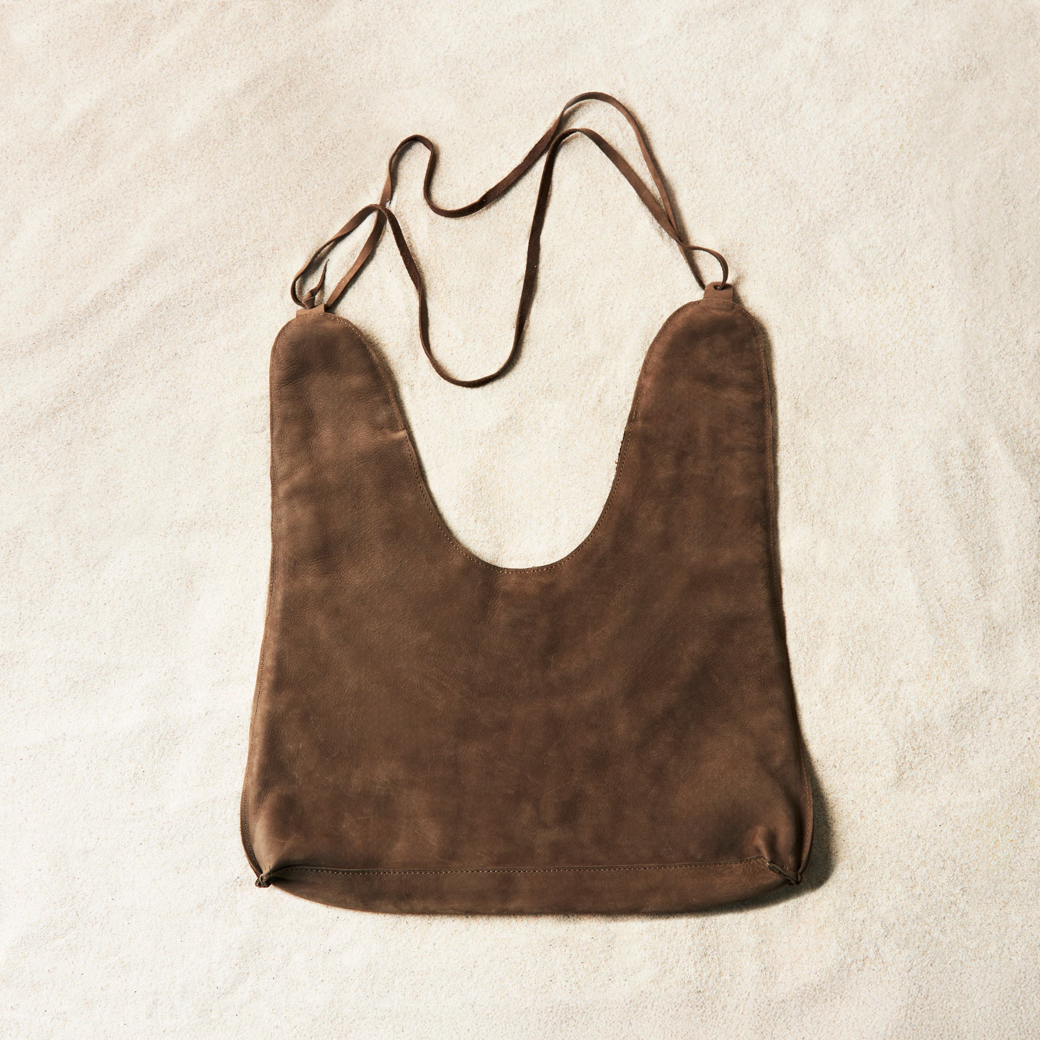 Back view of brown caramel suede leather bag on a sand background