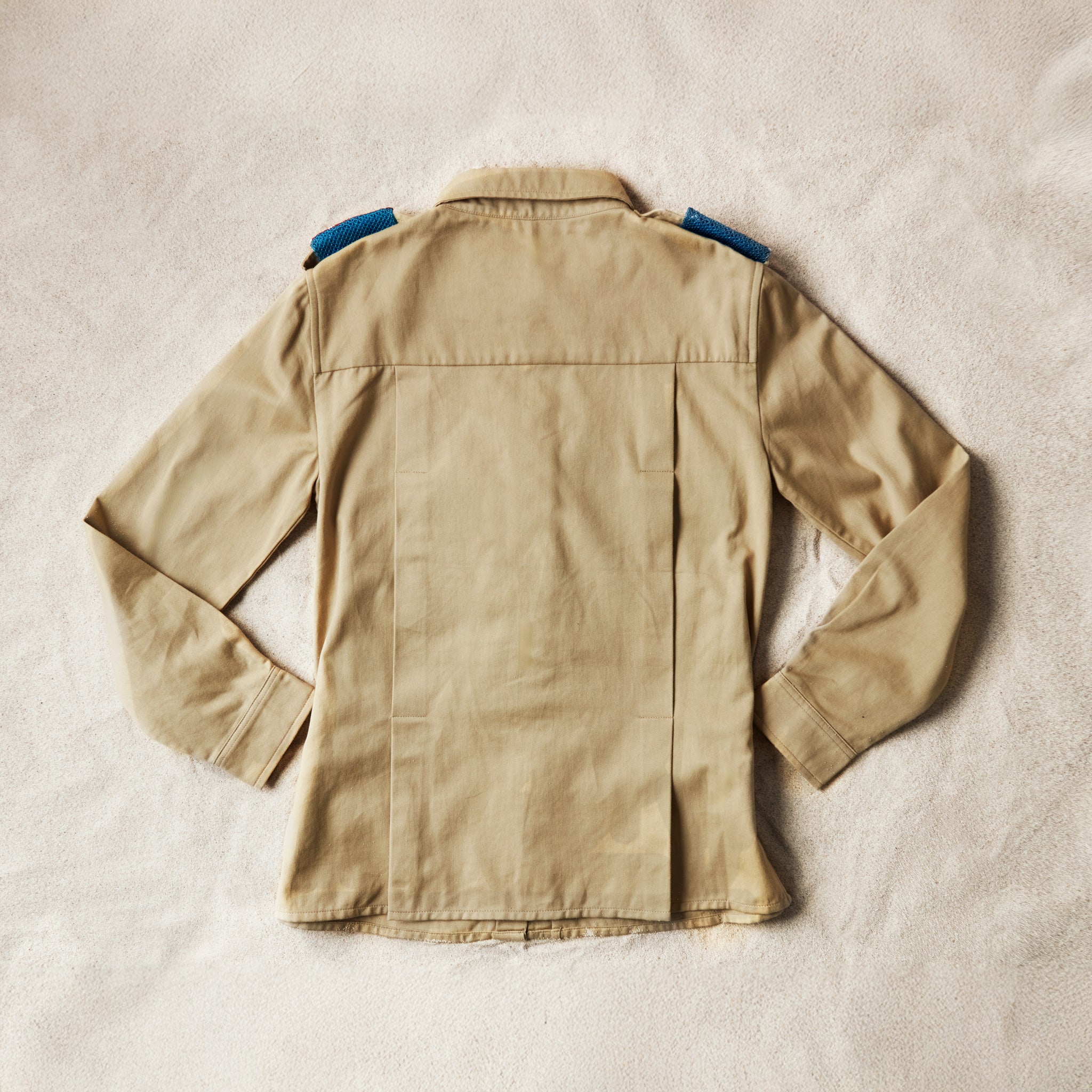 Flat back view of Khaki safari shirt on a sand background