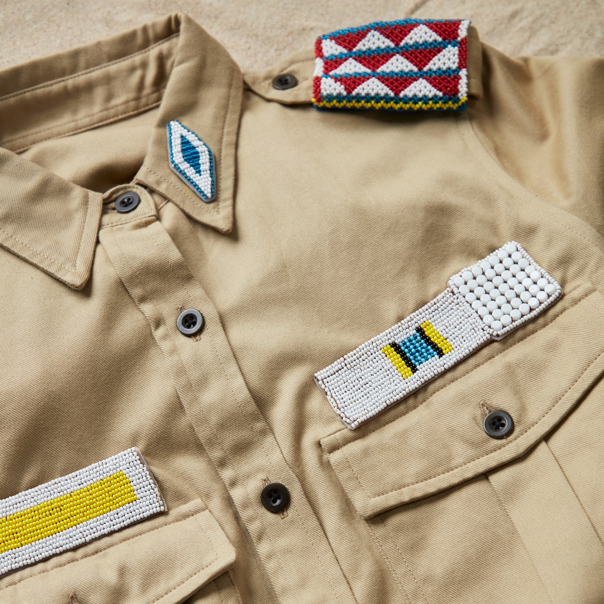 Detailed view of the colorful hand beaded patches on the khaki safari shirt with pockets