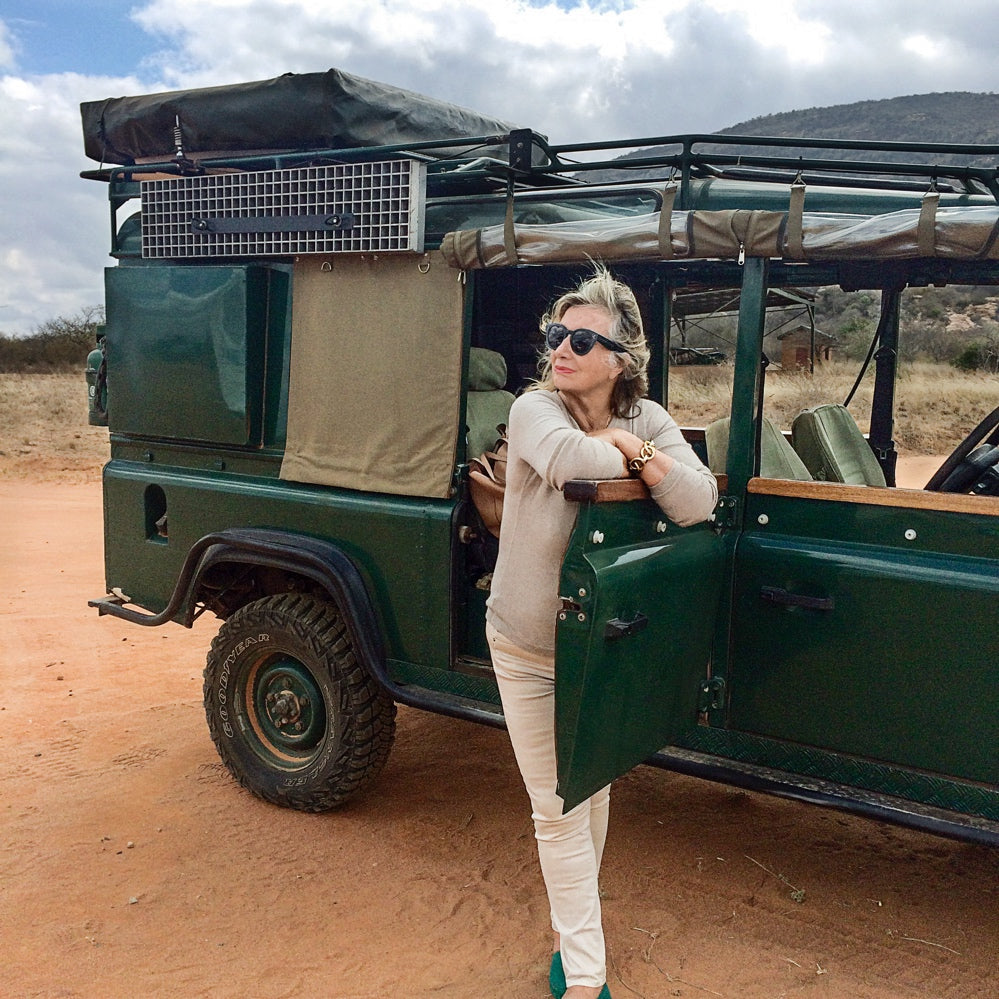 Woman in sunglasses standing next to a green safari vehicle in a desert setting