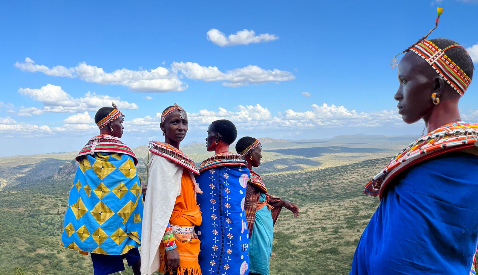 Samburu women in colorful attire, large colorful beaded neck pieces and headbands in front of a lands and sky of Kenya