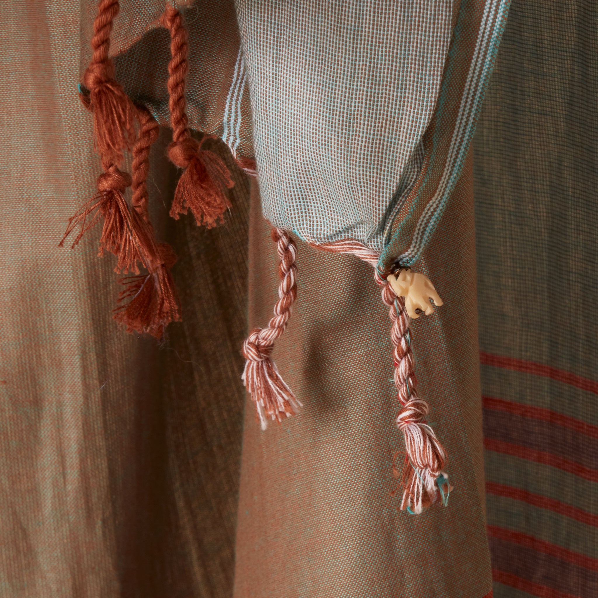 A close up of the twisted fringe of the brown and grey sarong/pareo featuring a small elephant charm.