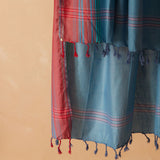A close up of the fringe of the red and teal blue cotton sarong/pareo against a warm beige background.