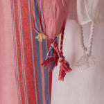 A close up of the fringe of the white and pink striped cotton pareo/sarong featuring a cream colored elephant charm.