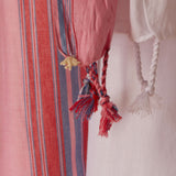 A close up of the fringe of the white and pink striped cotton pareo/sarong featuring a cream colored elephant charm.