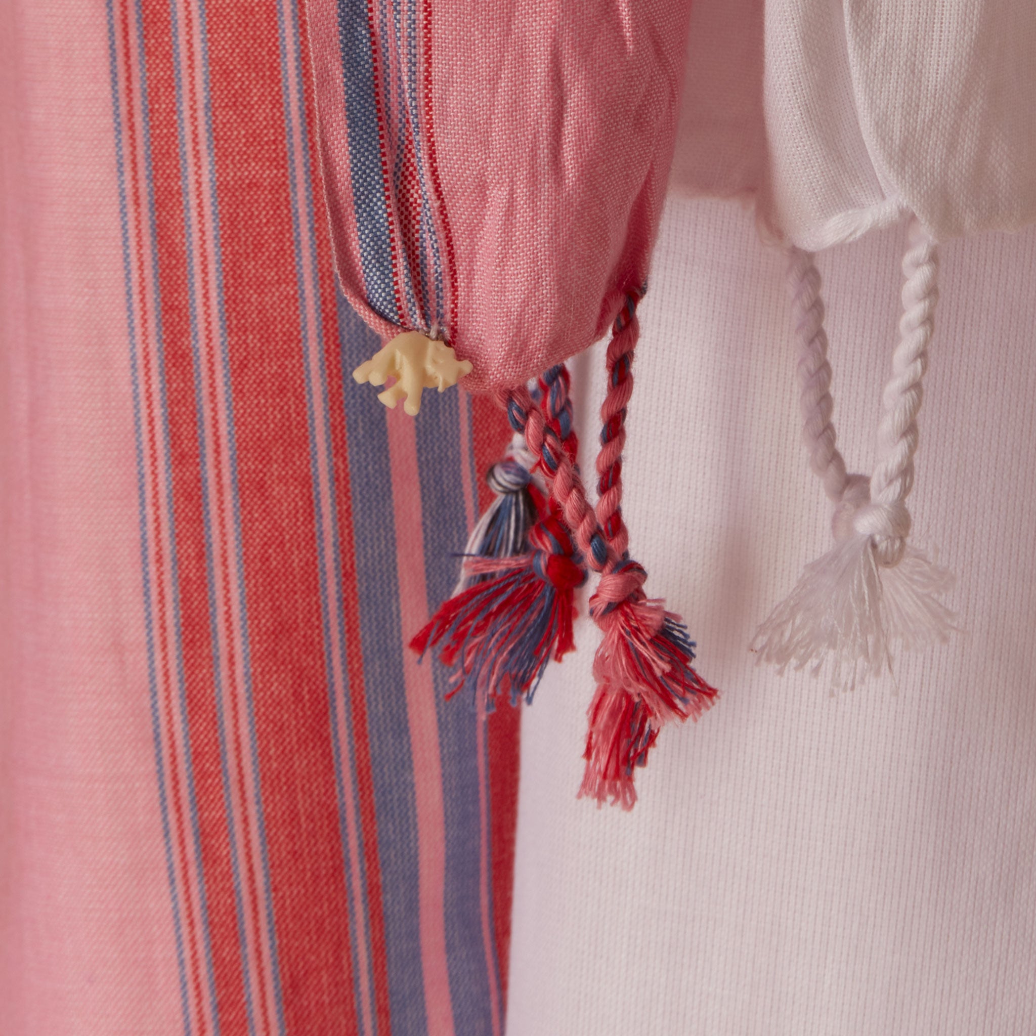 A close up of the fringe of the white and pink striped cotton pareo/sarong featuring a cream colored elephant charm.