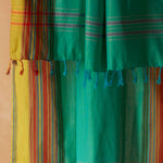 A close-up of a bright green sarong/pareo with yellow, red and orange plaid stripes featuring twisted/braided tassel fringe.