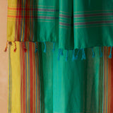A close-up of a bright green sarong/pareo with yellow, red and orange plaid stripes featuring twisted/braided tassel fringe.