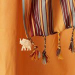 A close up of twisted fringe and a cream colored elephant charm  of a A yellow orange cotton pareo/sarong with multicolored striped borders.
