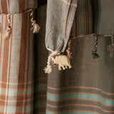 Close-up of a striped sarong/pareo  with braided tassels and a cream colored elephant charm.
