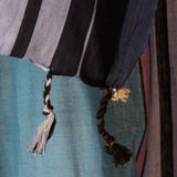 A close up of the tassel fringe and cream elephant charm of a teal blue and navy striped cotton pareo/sarong.