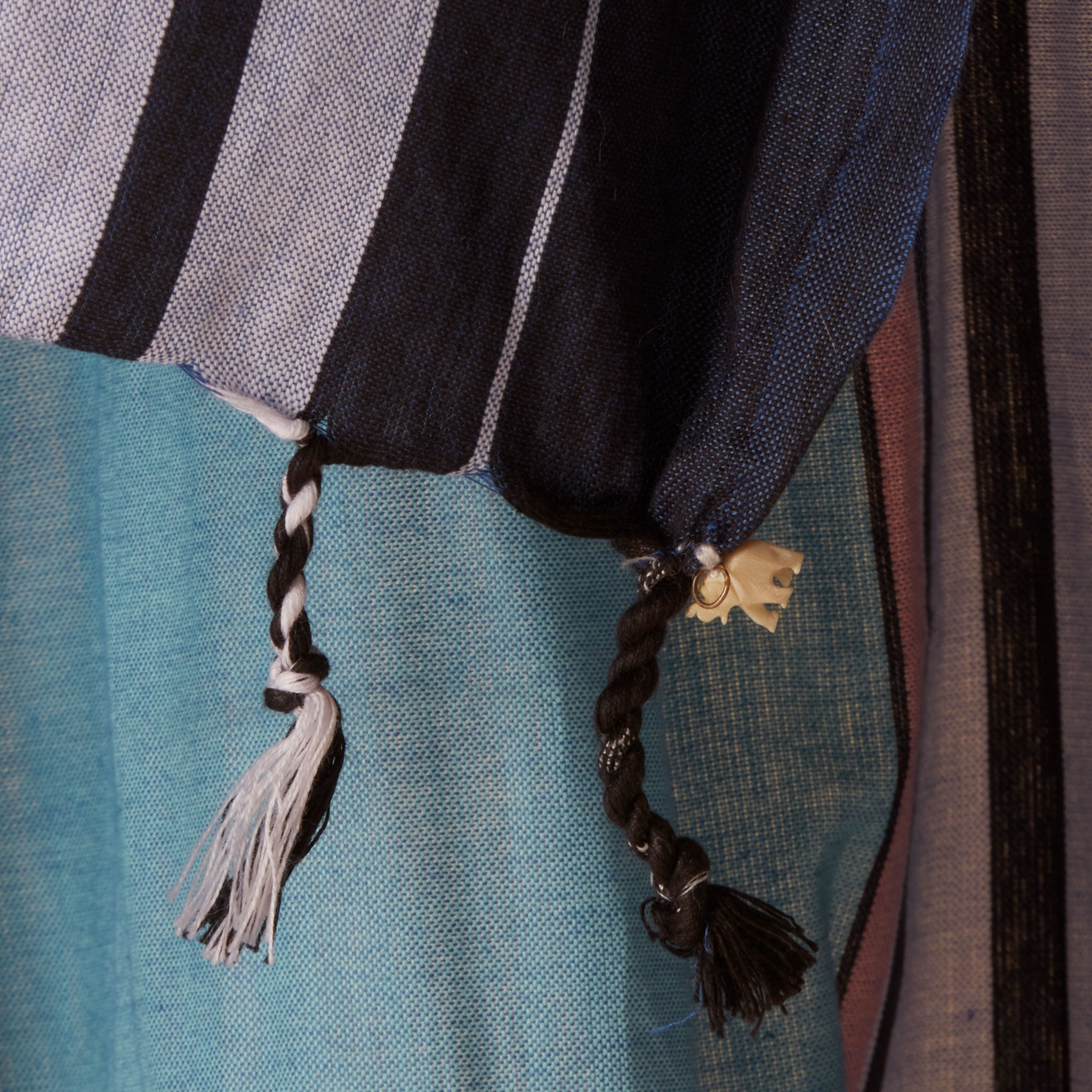 A close up of the tassel fringe and cream elephant charm of a teal blue and navy striped cotton pareo/sarong.