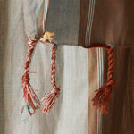 A close up of the tassel fringe with a cream elephant charm of pareo/sarong in grey and brown with red striped bands