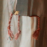 A close up of the tassel fringe with a cream elephant charm of pareo/sarong in grey and brown with red striped bands