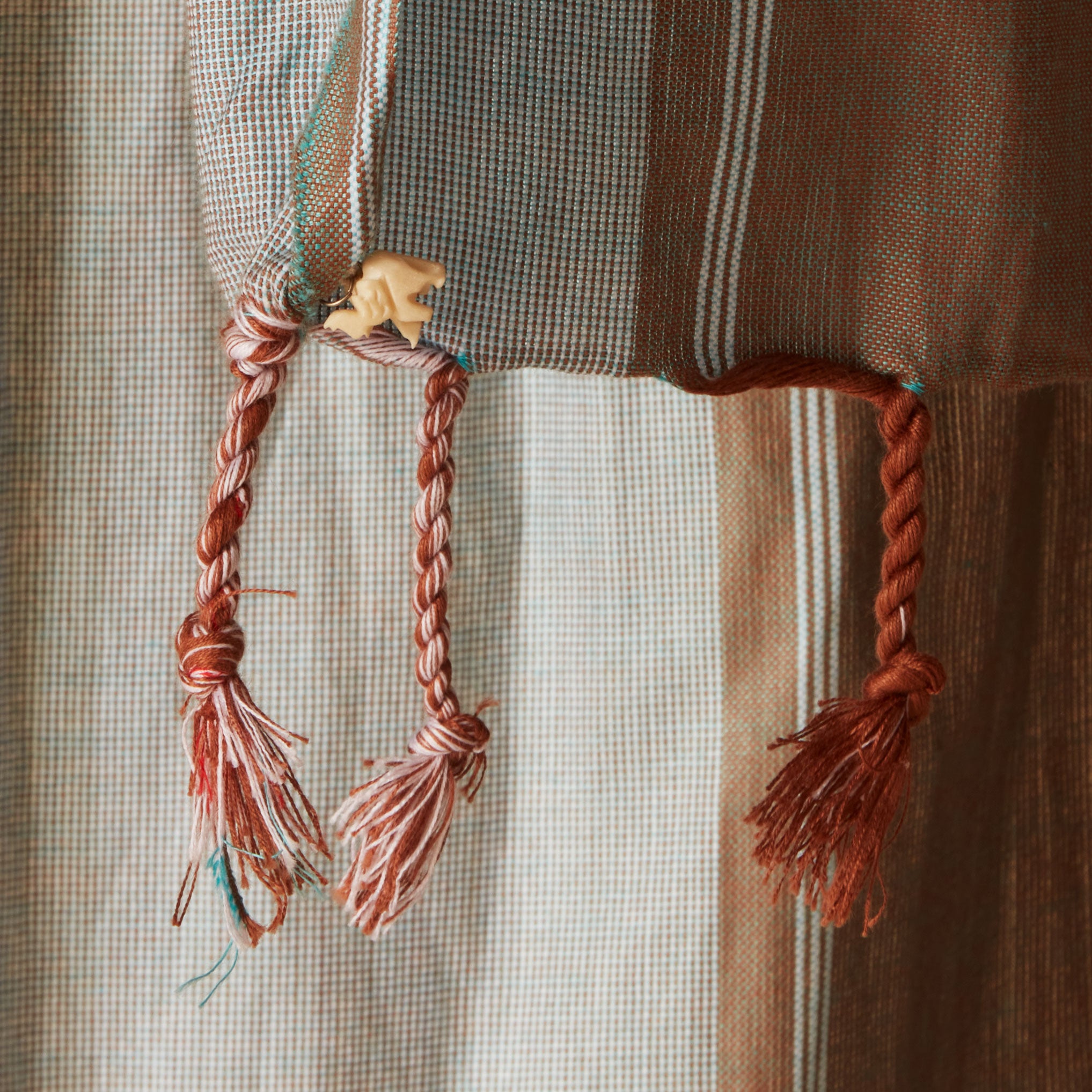 A close up of the tassel fringe with a cream elephant charm of pareo/sarong in grey and brown with red striped bands