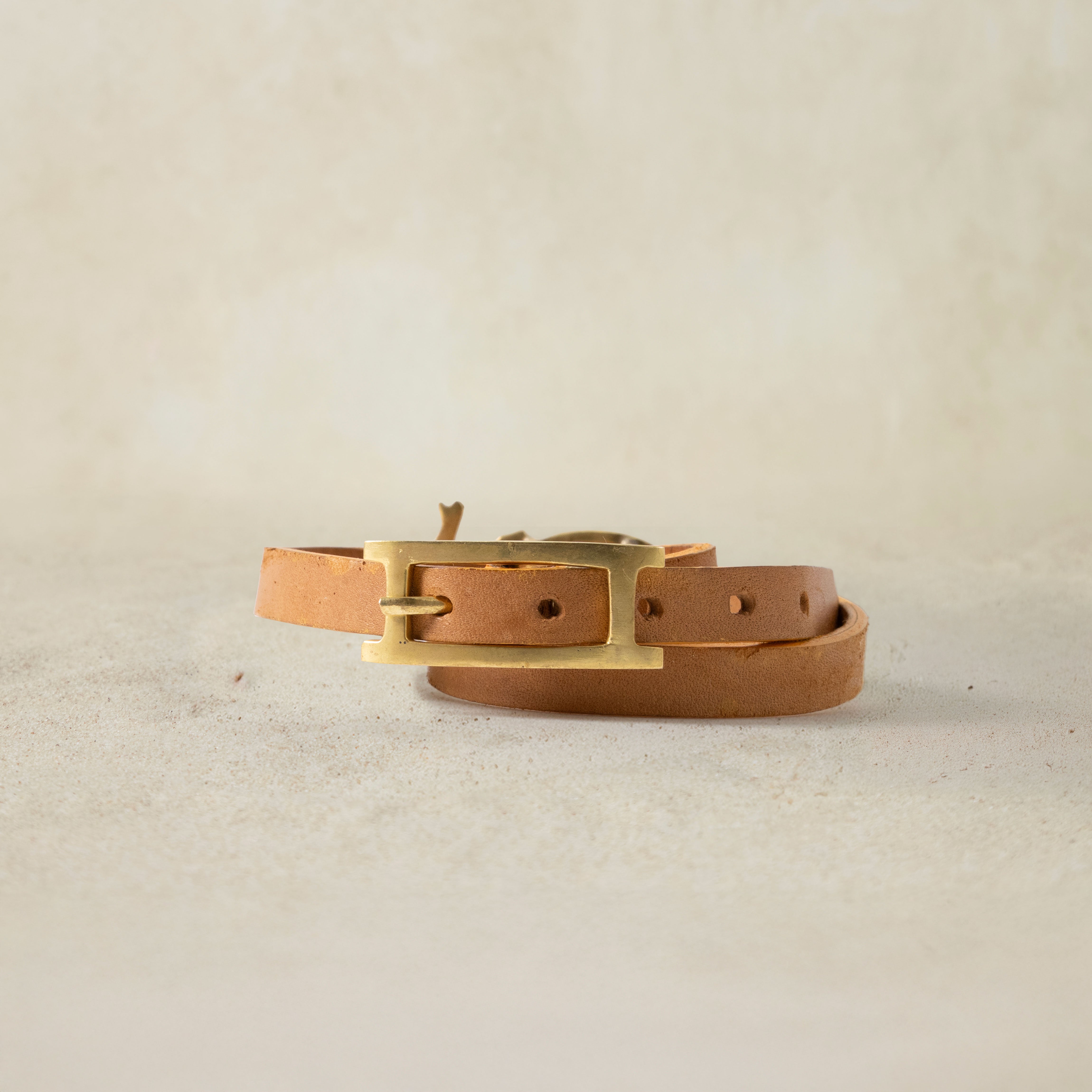 Back View of brown leather bracelet with brass elephant and brass buckle closure on a sand background