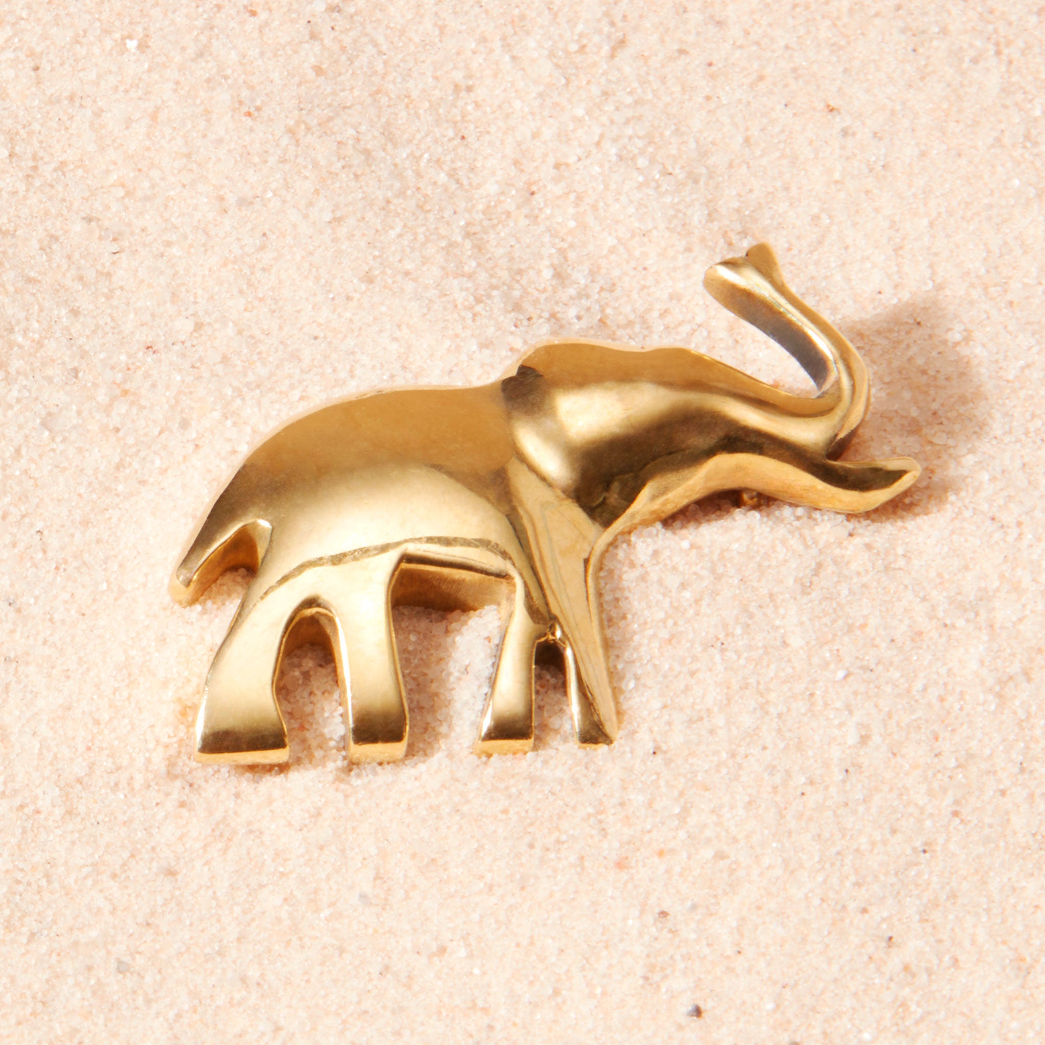 Brass elephant pin on a sand background