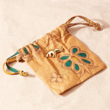 Drawstring pouch with floral patterns and a brass elephant pin on a beige background