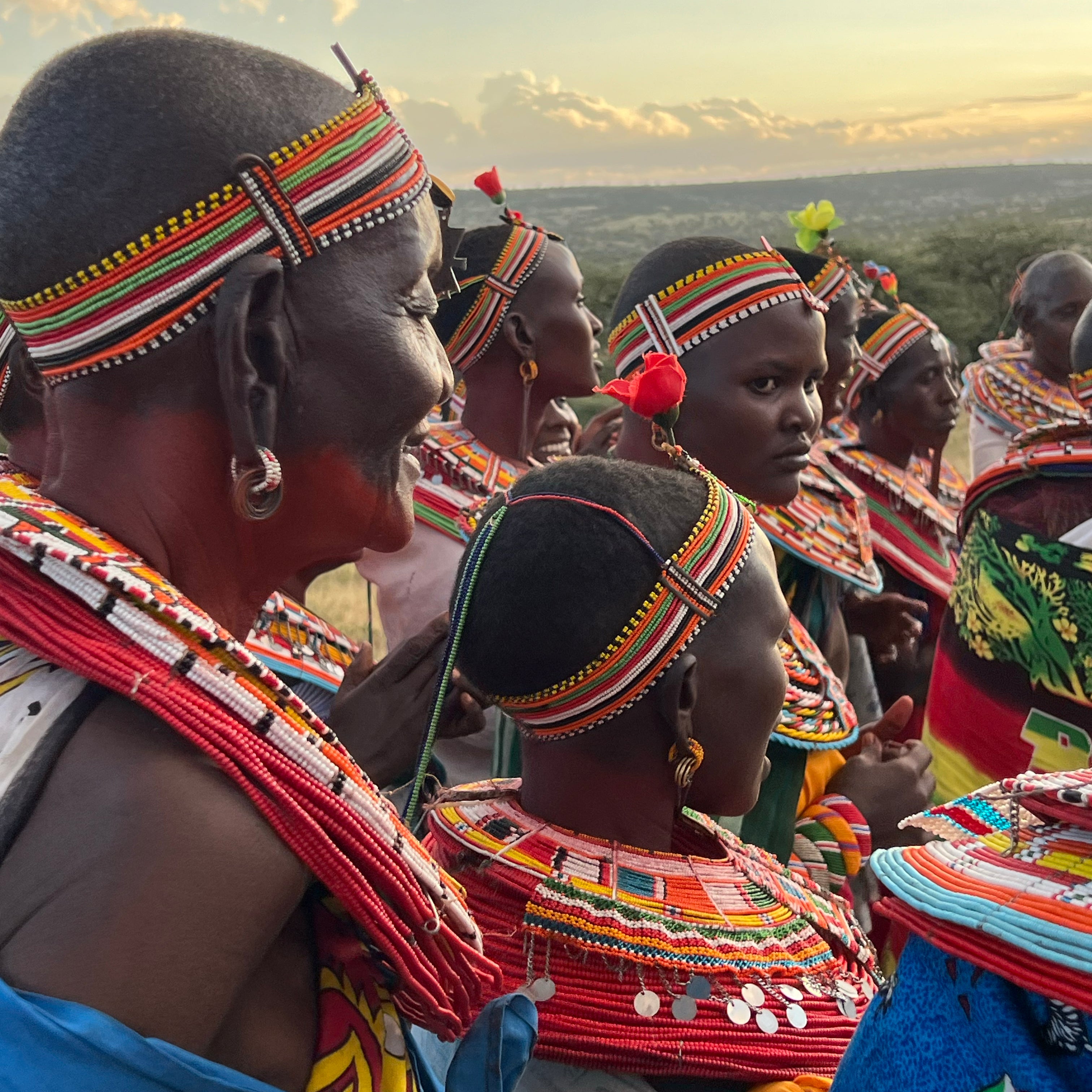 Group of Samburu people in traditional attire with colorful headbands and clothing, standing together with a horizon in the background