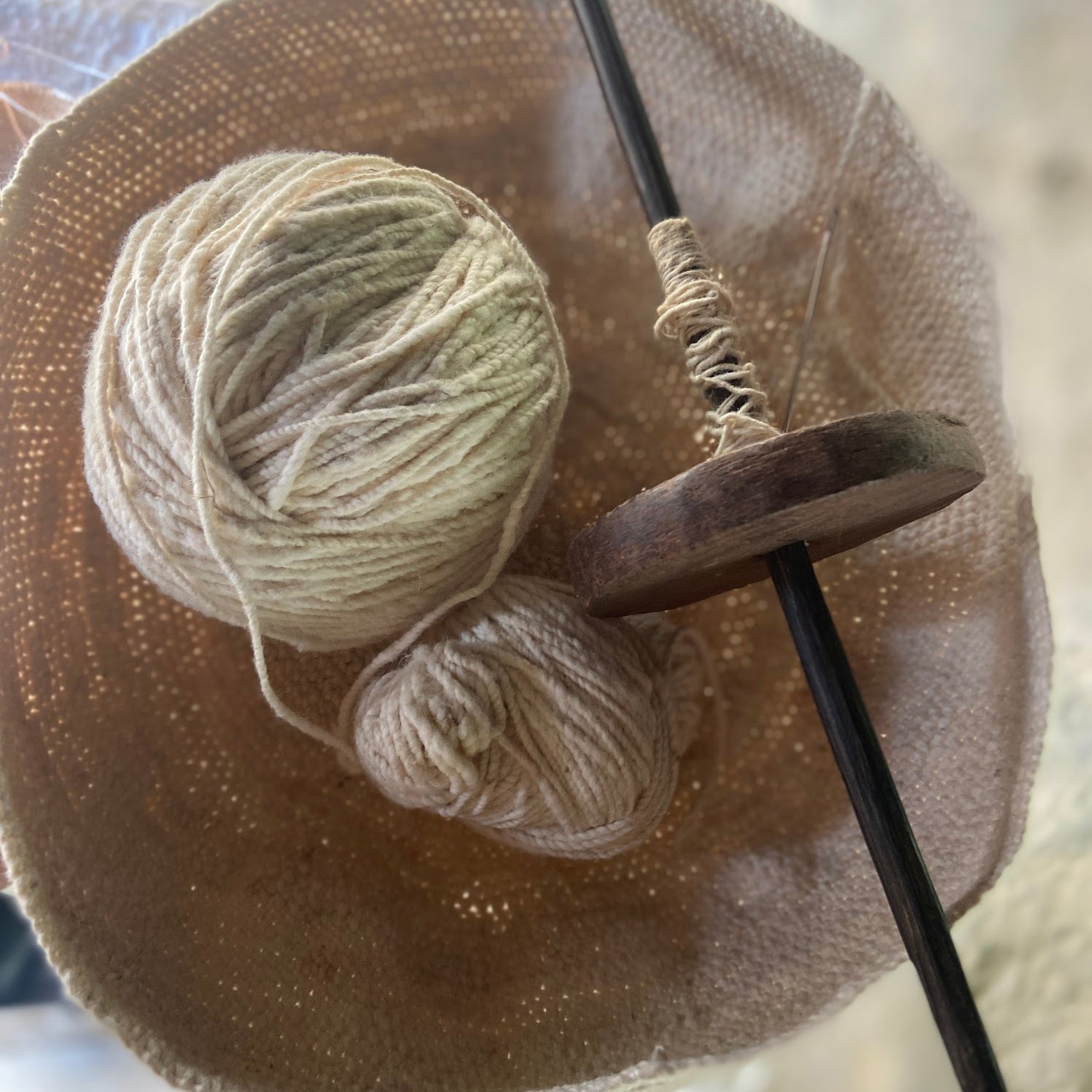 Ball of yarn with  a wooden spinning wheel with a black spindle in a woven bag 