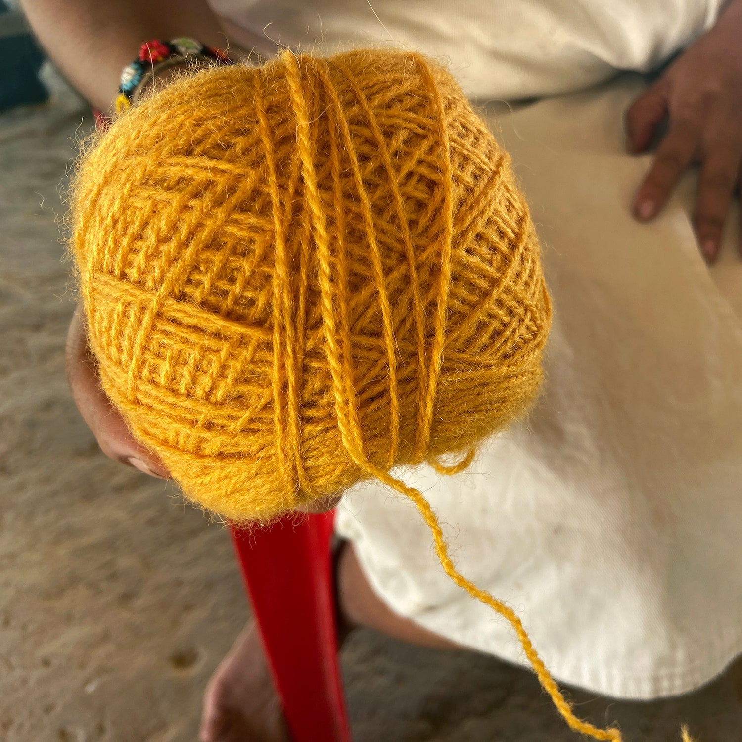 Close up view of a yellow yarn ball held by a person sitting in a red chair with a blurred background