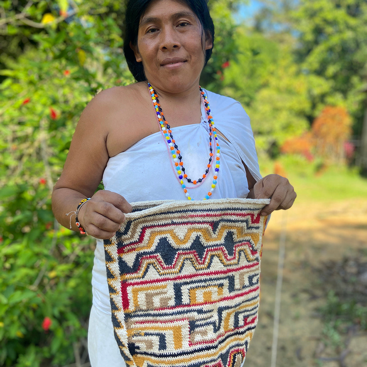 Woman holding a colorful woven mochila bag outdoors with a lush green background