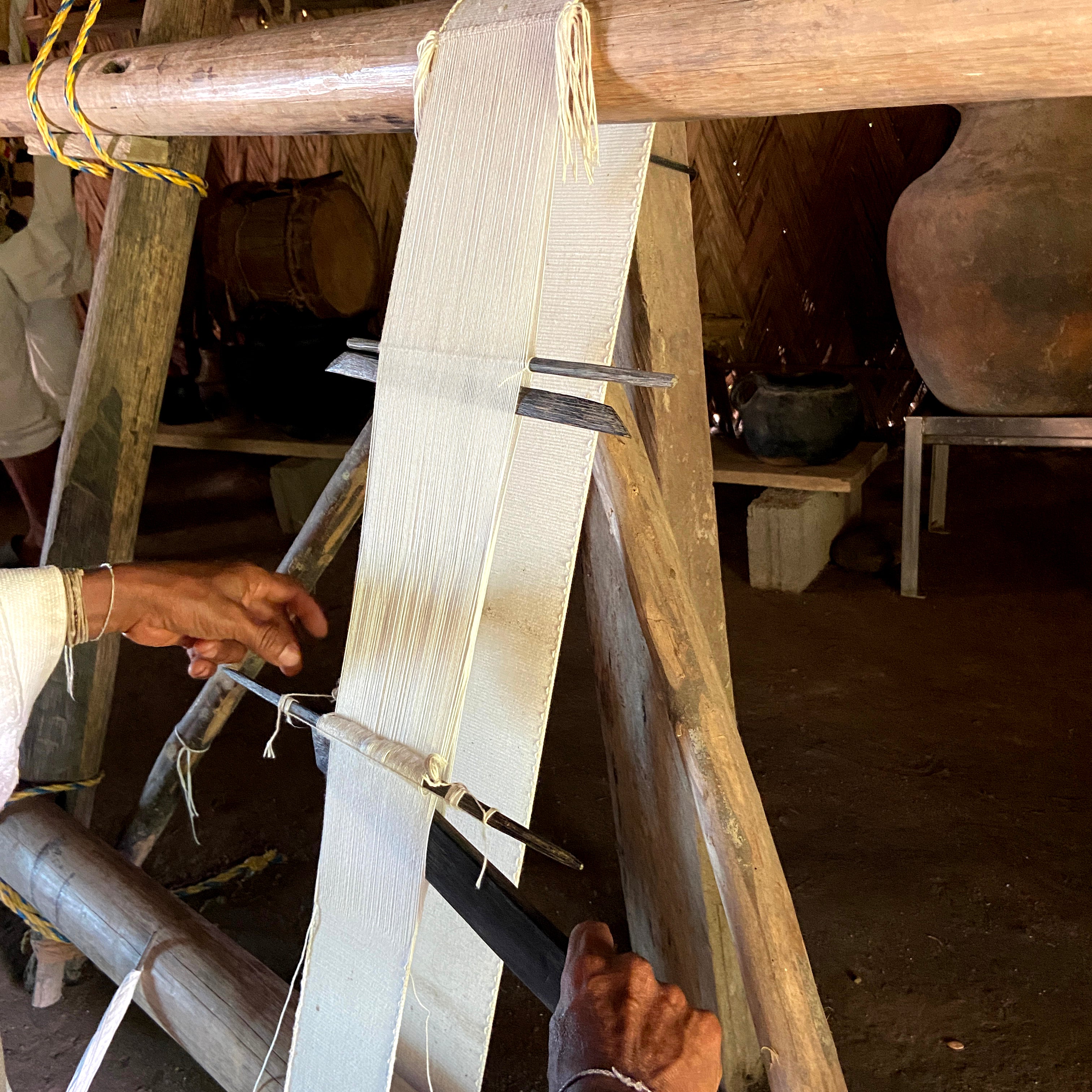 Person using a traditional loom with wooden beams to weave cotton fibers into fabric