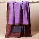 A purple towel draped over a rustic wooden branch showing the reddish brown, blue floral patterned side of the towel.