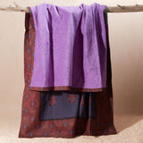 A purple towel draped over a rustic wooden branch showing the reddish brown, blue floral patterned side of the towel.