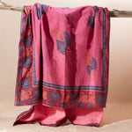 A pink kanga towel with one fabric side featuring a fine dotted pattern, a blue border, and orange and blue leaf motifs with a pink terry cloth towel lining.