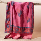 A pink kanga towel with one fabric side featuring a fine dotted pattern, a blue border, and orange and blue leaf motifs with a pink terry cloth towel lining.