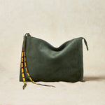 Large olive green suede leather pouch bag with yellow, black, and red beaded zipper pull ties on a sand background
