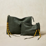 Two olive green suede leather bags in different sizes with yellow, black, and red beaded zipper pull ties on a sand background