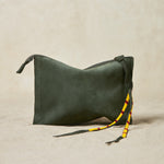Small olive green suede leather pouch bag with yellow, black, and red beaded zipper pull ties on a sand background
