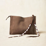 Small sand brown suede leather pouch bag with white, black, and red beaded zipper pull ties on a sand background