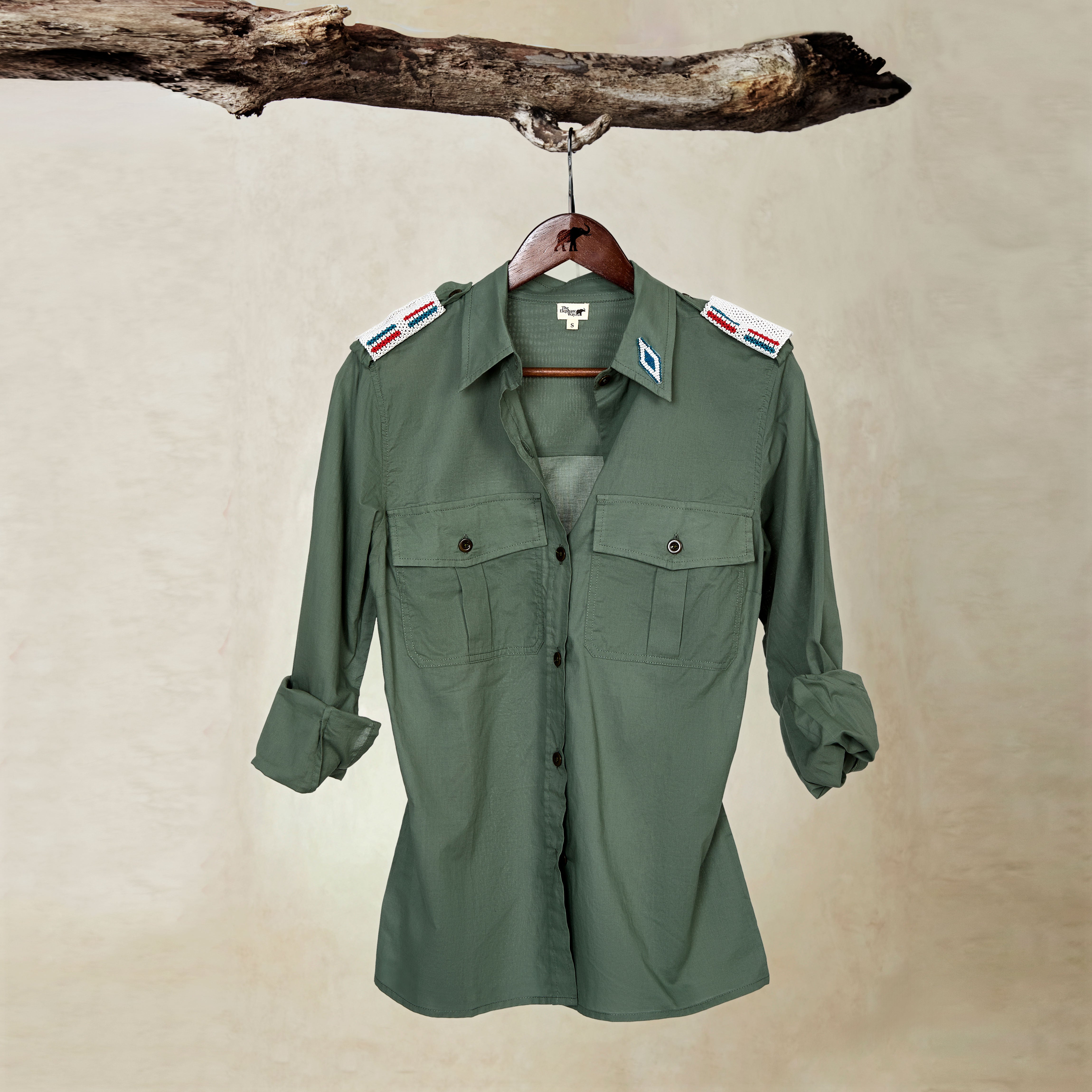 Khaki Green Lightweight Ranger Shirt with White and Colorful Beaded Epaulettes on a hanger from a branch