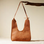 Back view of leather handbag with a strap on a branch on a beige background