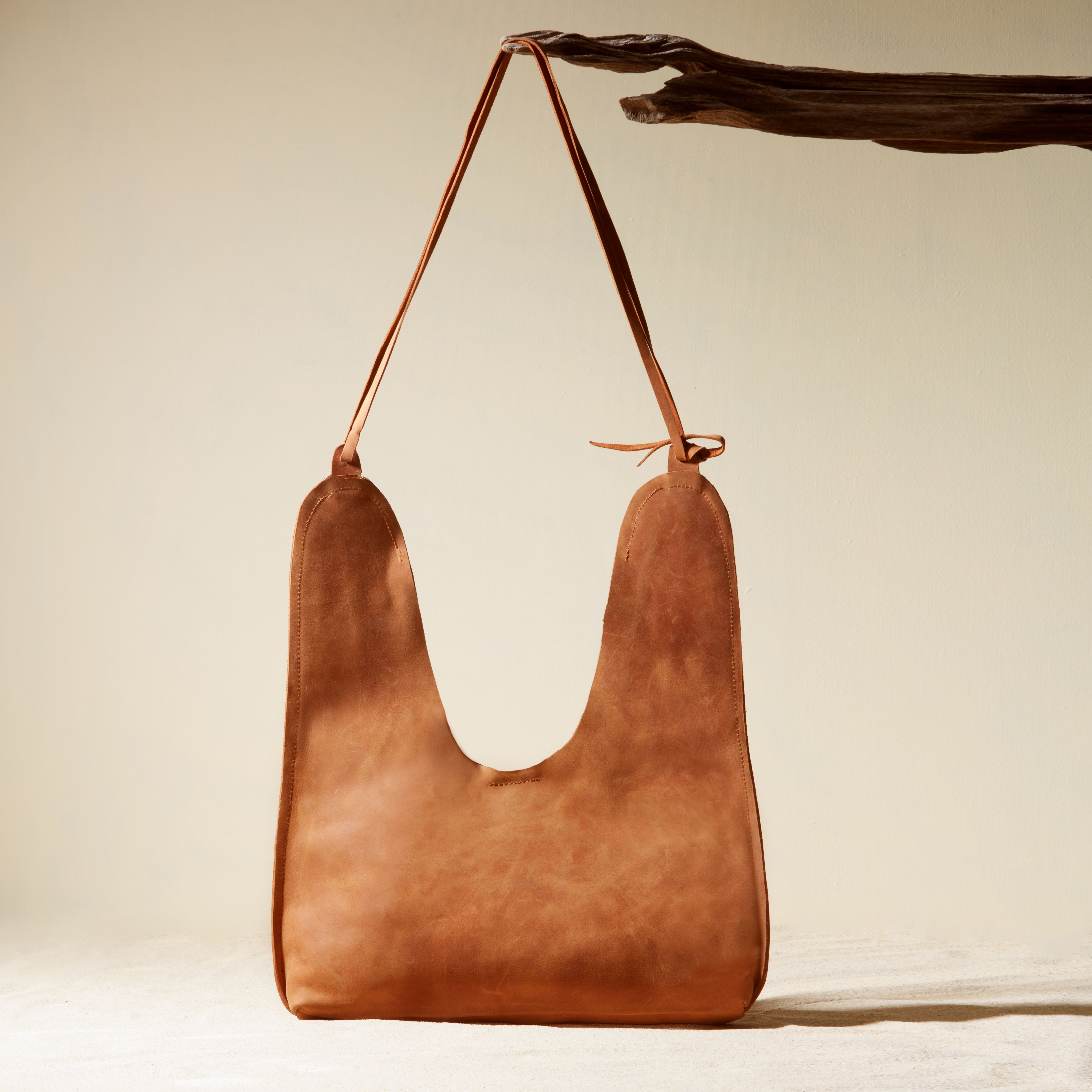 Back view of leather handbag with a strap on a branch on a beige background