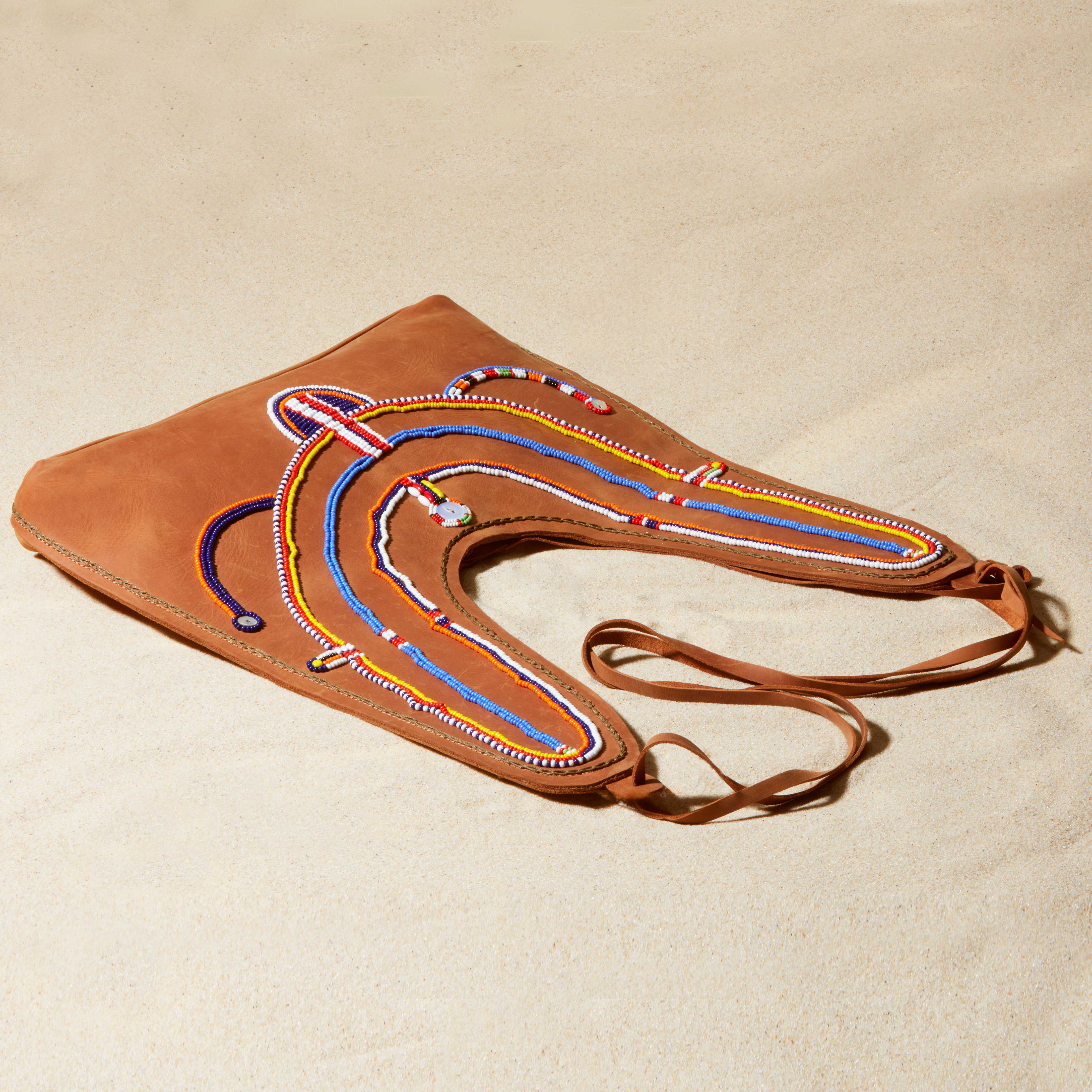 Brown leather handbag with colorful beadwork lying flat on a beige sand background