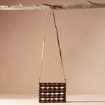 Beaded handbag with a geometric pattern and a brown leather strap hanging on a branch