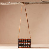 Beaded handbag with a geometric pattern and a brown leather strap hanging on a branch
