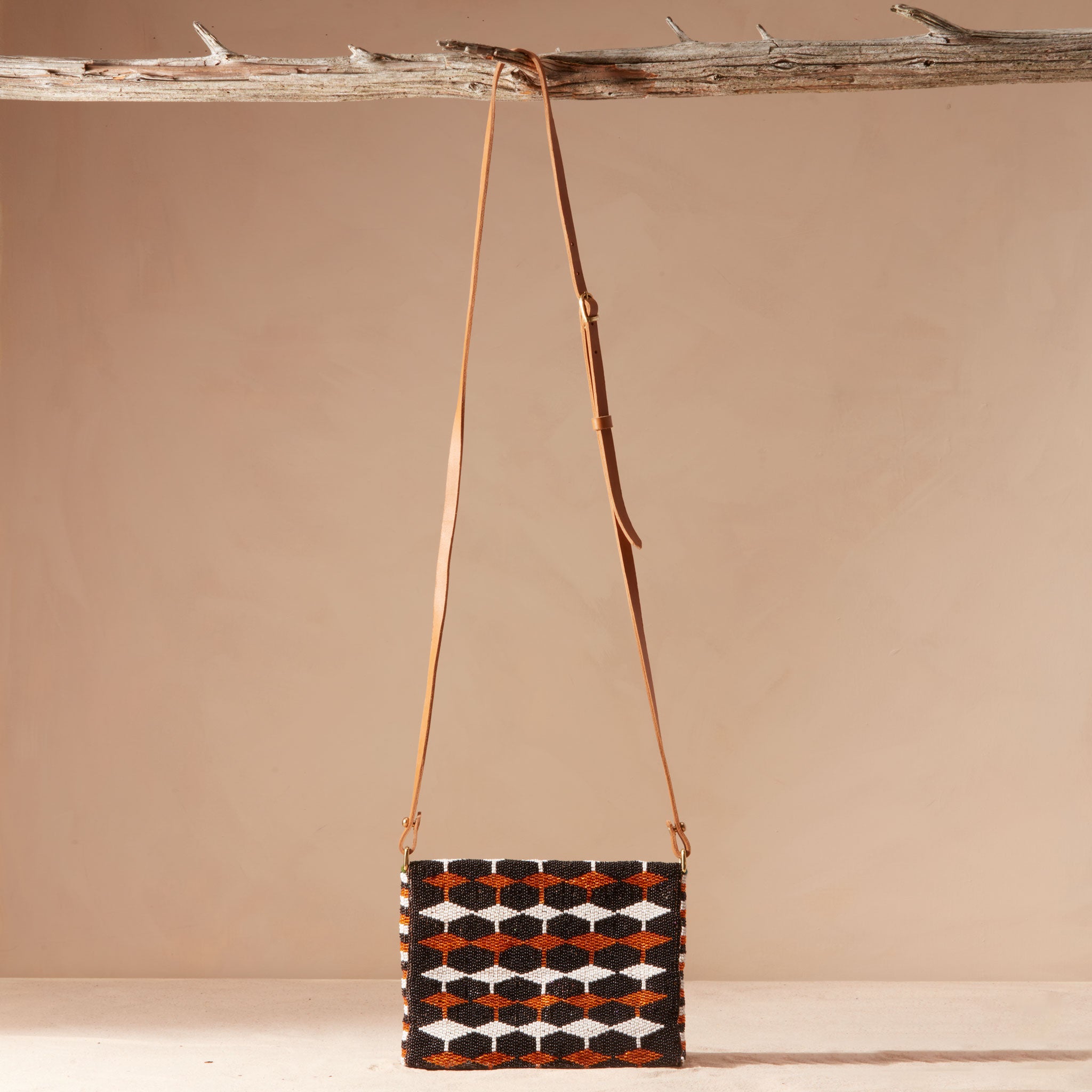 Beaded handbag with a geometric pattern and a brown leather strap hanging on a branch