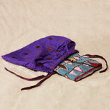 Colorful beaded clutch inside a vibrant purple kanga fabric dust bag on a sandy surface