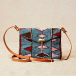 Handmade beaded bag with geometric pattern and elephant charm and brown leather strap on a beige background