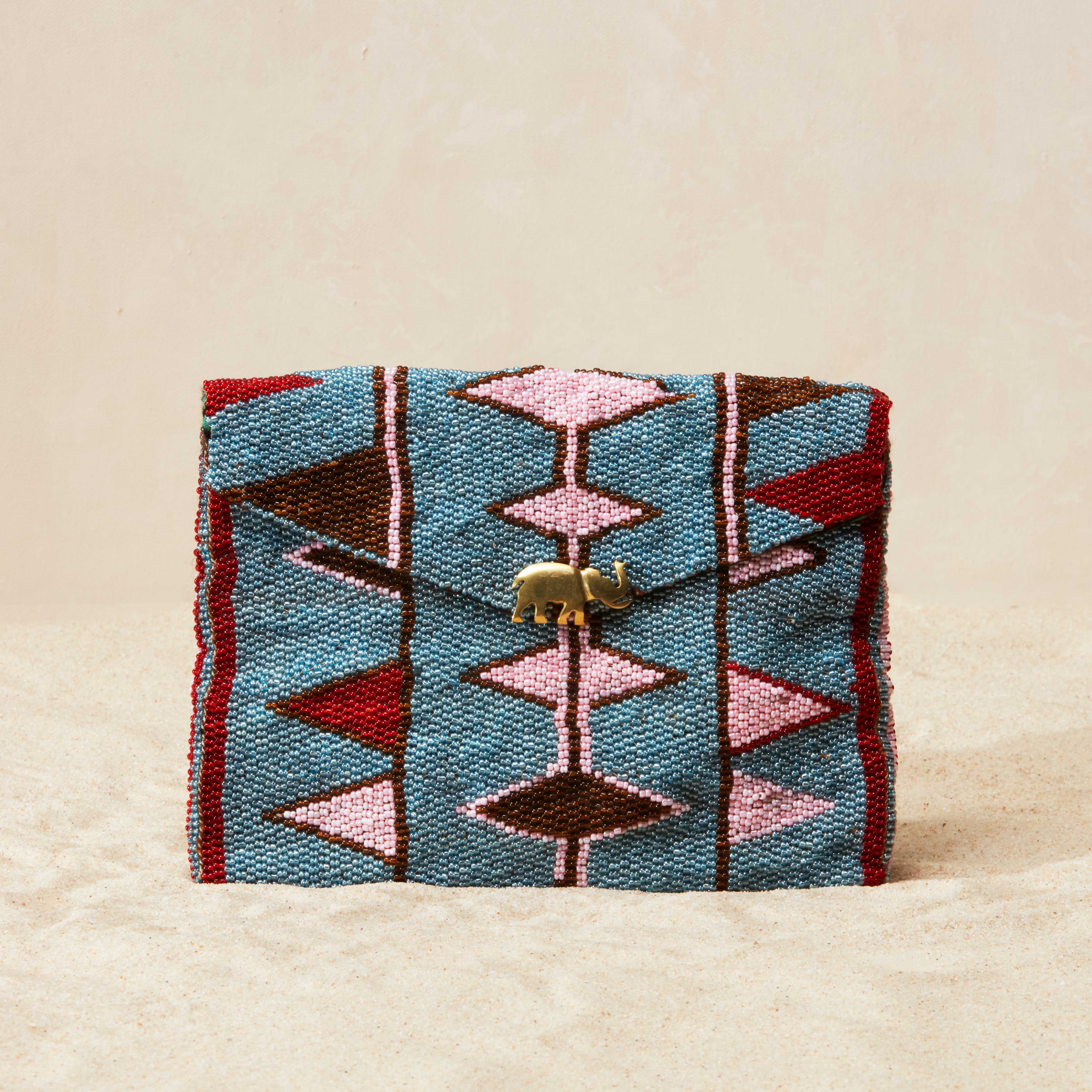 Colorful beaded pouch with geometric pattern and a brass elephant emblem on beige background